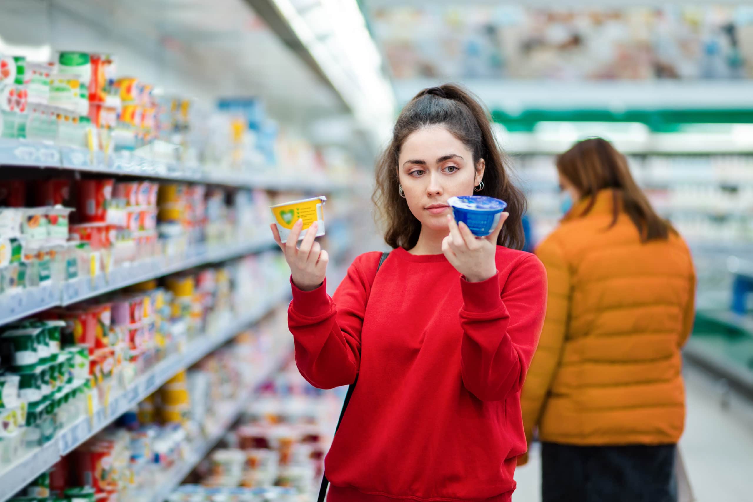 A woman compares two different packages of yogurt in a supermarket.