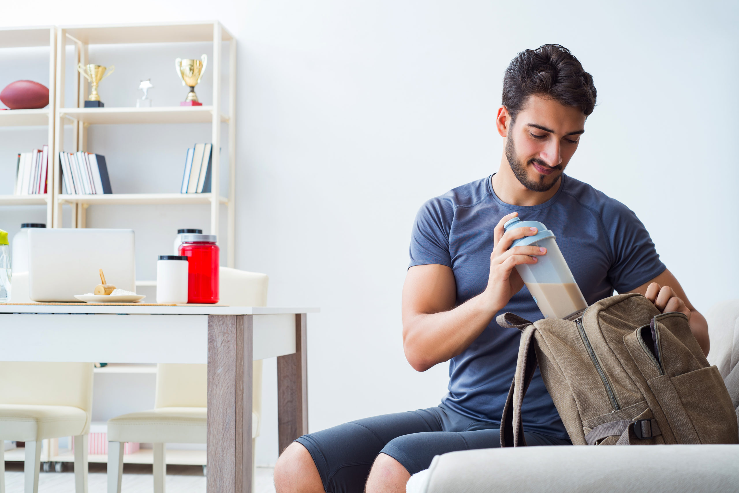 A man dressed in sportswear preparing to exercise placing a milkshake in his backpack.